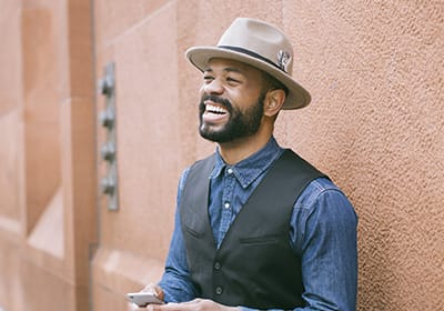 man in nice clothes standing against wall checking his phone and smiling